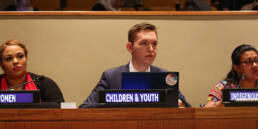 Thee civil society delegates sitting in the Plenary at the UN headquarters, waiting for their turn to deliver an intervention. On the three monitors infront of them it reads: women, children & youth, Indigenous Peoples