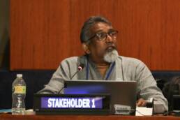 Paul Divakar Namala, Convenor, Global Forum of Communities Discriminated on Work and Descent speaking into a microphone looking to his left at HLPF
